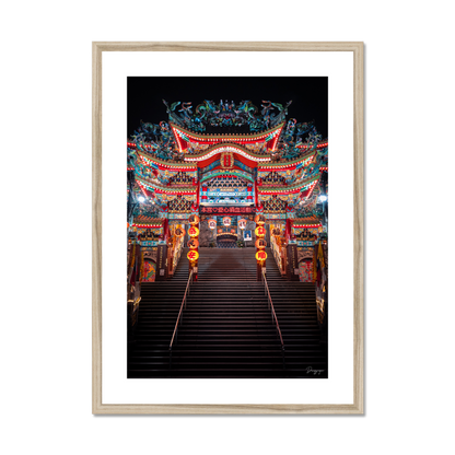 Framed art in a beige  wooden frame showing a very impressive Taoist temple with lights that are glowing in the night in Taipei Taiwan