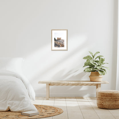 Mockup of wall art showing a small beige wooden frame that is hanging on the wall of a bedroom and contains a photo of the Parthenon on the hill of Acropolis in Athens Greece